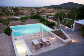 Una piscina con cubierta de piedra, dos sillas de descanso y una pequeña mesa.