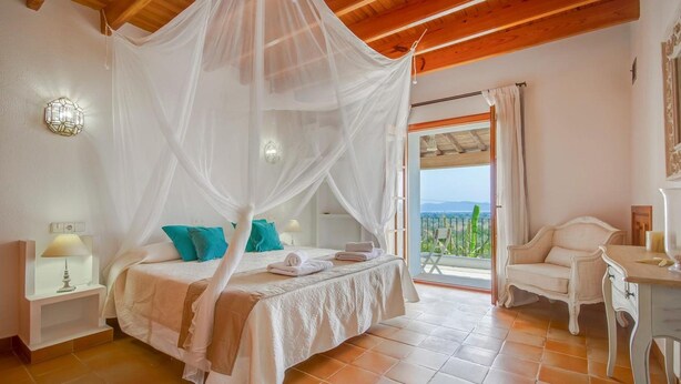 A bedroom with a bed under a canopy, a nightstand, a desk, and a view of the outdoors.