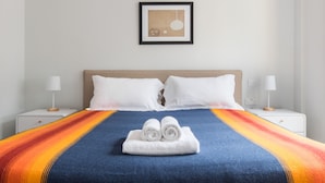 Une chambre d’hôtel avec un grand lit, deux oreillers blancs, une couvre-lit à rayures bleues et oranges, et un tableau encadré accroché au mur.
