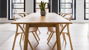 A modern dining area with a wooden table and chairs, a potted plant, and large windows with black frames. - Vibrant Leicester Square 2BR - Netflix Nespresso (London)
