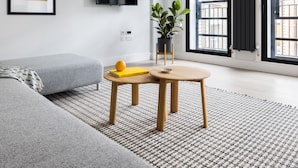 A modern living room with a grey sofa, a small wooden table with a book and an orange, a potted plant, and a flat-screen TV mounted on the wall. - Vibrant Leicester Square 2BR - Netflix Nespresso (London)