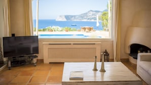 Sala de estar com televisão, lareira, mesa de centro com um livro e vista para o mar.