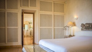 Quarto de hotel com uma cama grande, mesa com tampo de vidro, luminária e um objeto decorativo na parede.