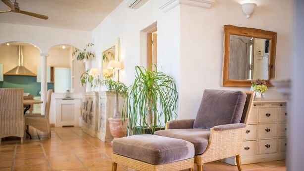 A spacious living room with a wicker armchair and ottoman, a dining area with a table and chairs, and a kitchen in the background. - Exclusiva Villa Vista mar 100 mt de Blue Marlin (Sant Josep de sa Talaia)