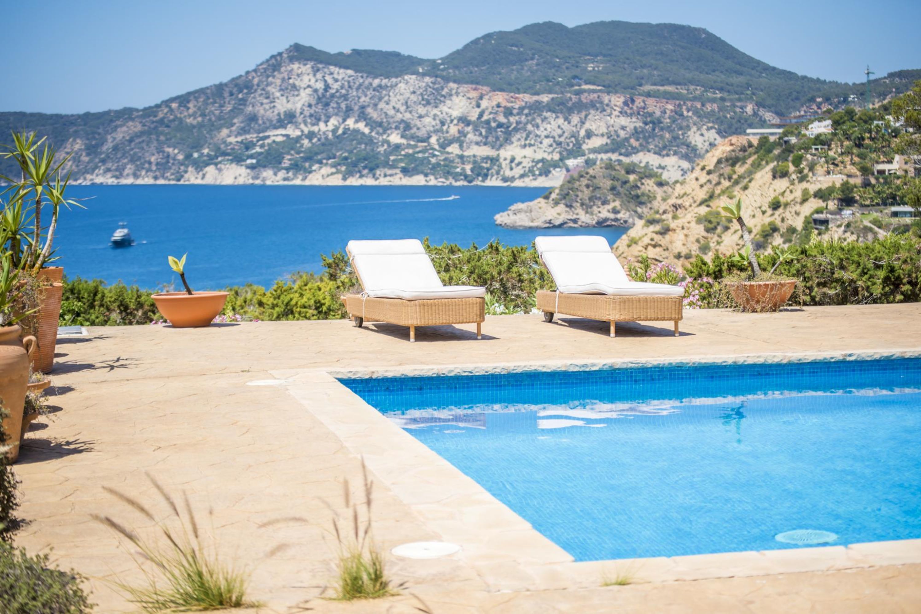 A pool area with two lounge chairs and potted plants.