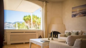 Uma sala de estar com sofá branco, uma mesa de centro e vista para o exterior através de uma grande janela.