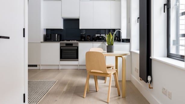 A modern kitchen with white cabinets, a built-in oven, a dining table with chairs, a potted plant, and a window with a view. - Cool Leicester Sq Studio - Netflix Nespresso (London)