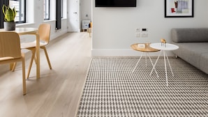 A modern living room with a flat-screen TV mounted on the wall, a grey sofa, a small round table with a white base, and a patterned rug. - Cool Leicester Sq Studio - Netflix Nespresso (London)