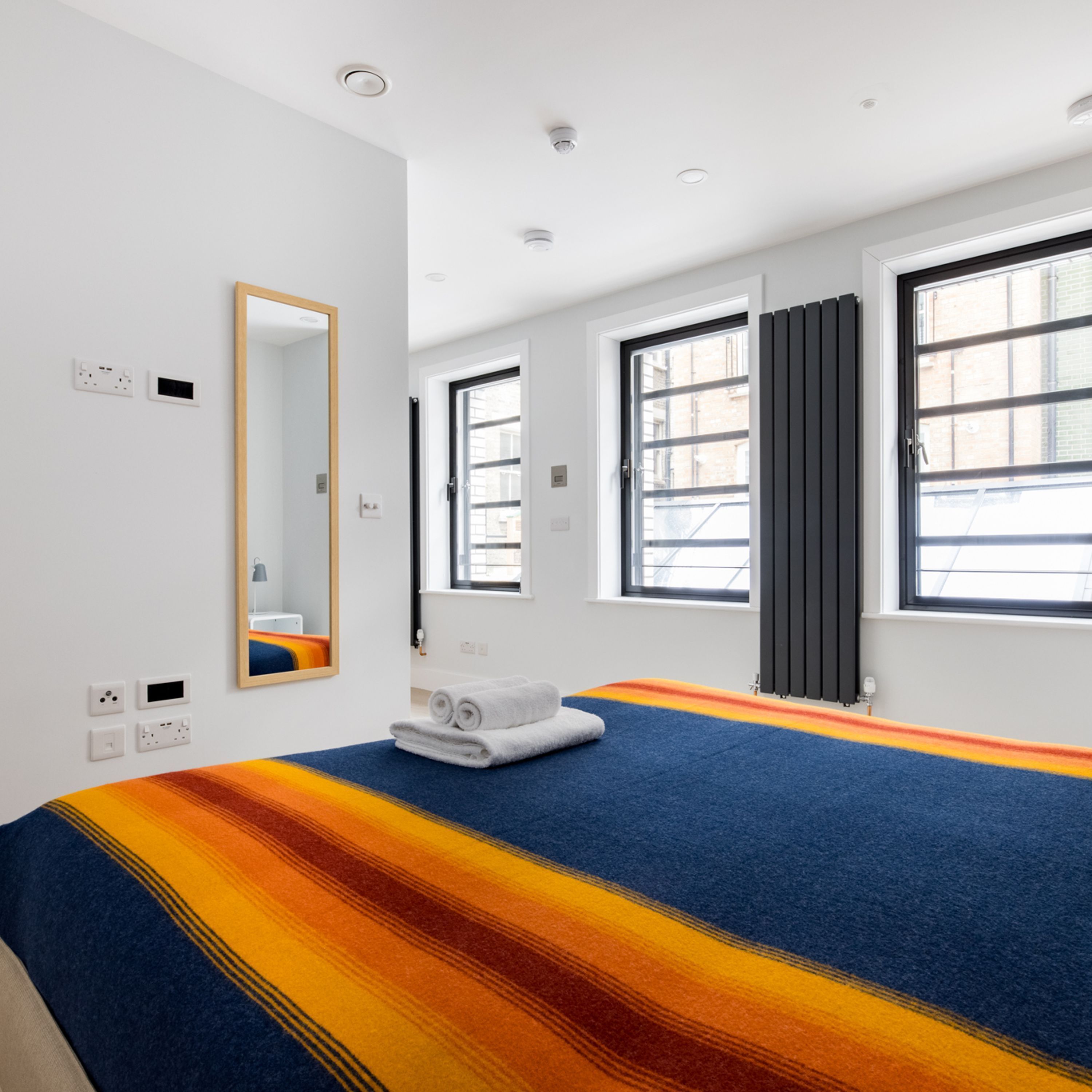 A modern hotel room with a large bed, a mirror, a window with curtains, and a view of the city.