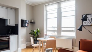 A modern living room with a dining area, a kitchen, and a large window providing natural light.