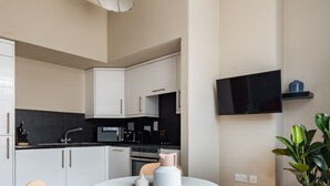 A modern kitchen with white cabinets, a black countertop, and a round wooden table with two chairs.