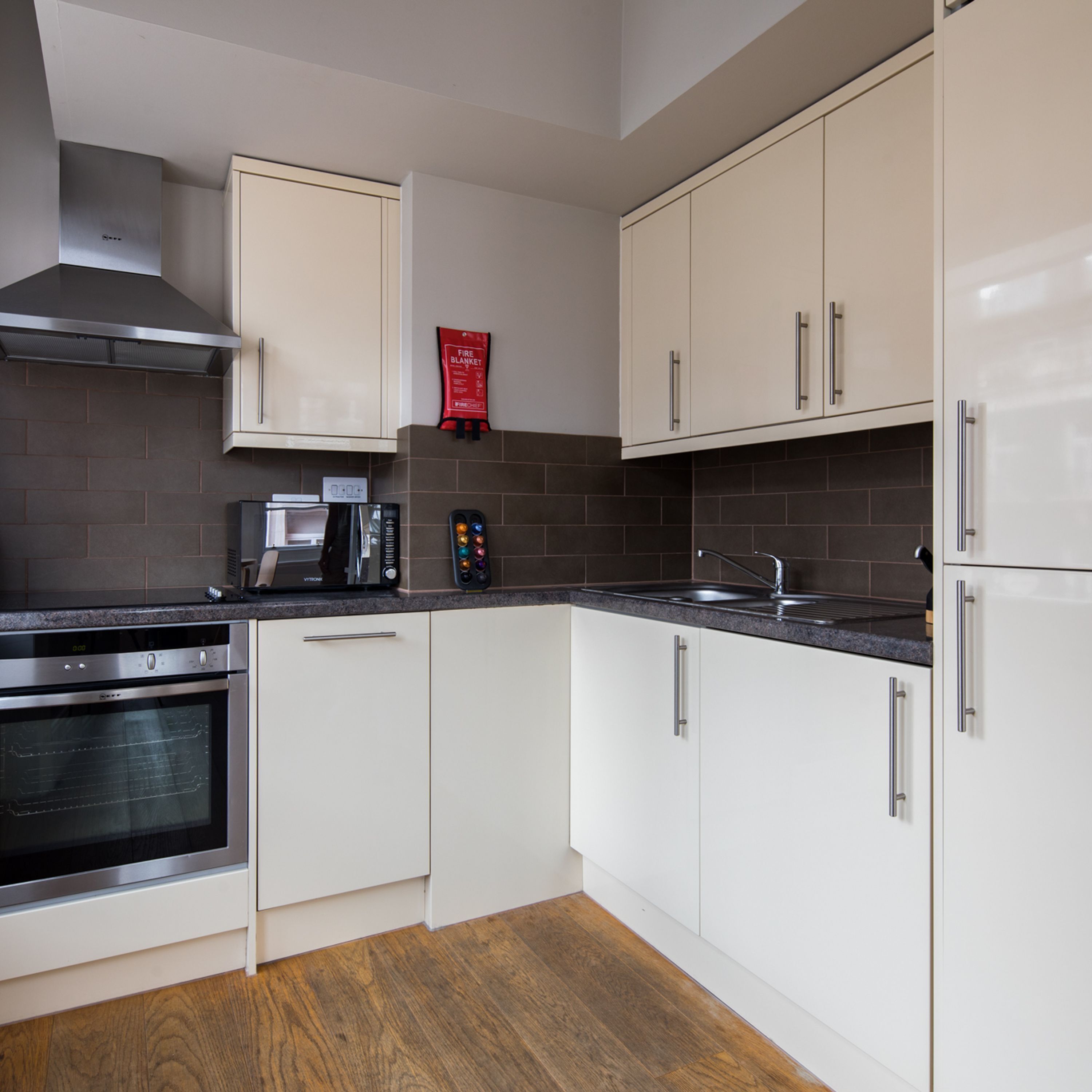 A modern kitchen with white cabinets, a stainless steel range hood, a microwave, and a built-in oven.