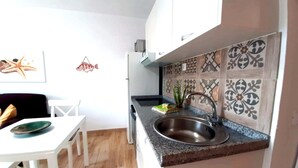 Cuina compacta amb taulell de granat, rentaplat amb acer inoxidable i zona de menjador amb taula i cadires blanques.