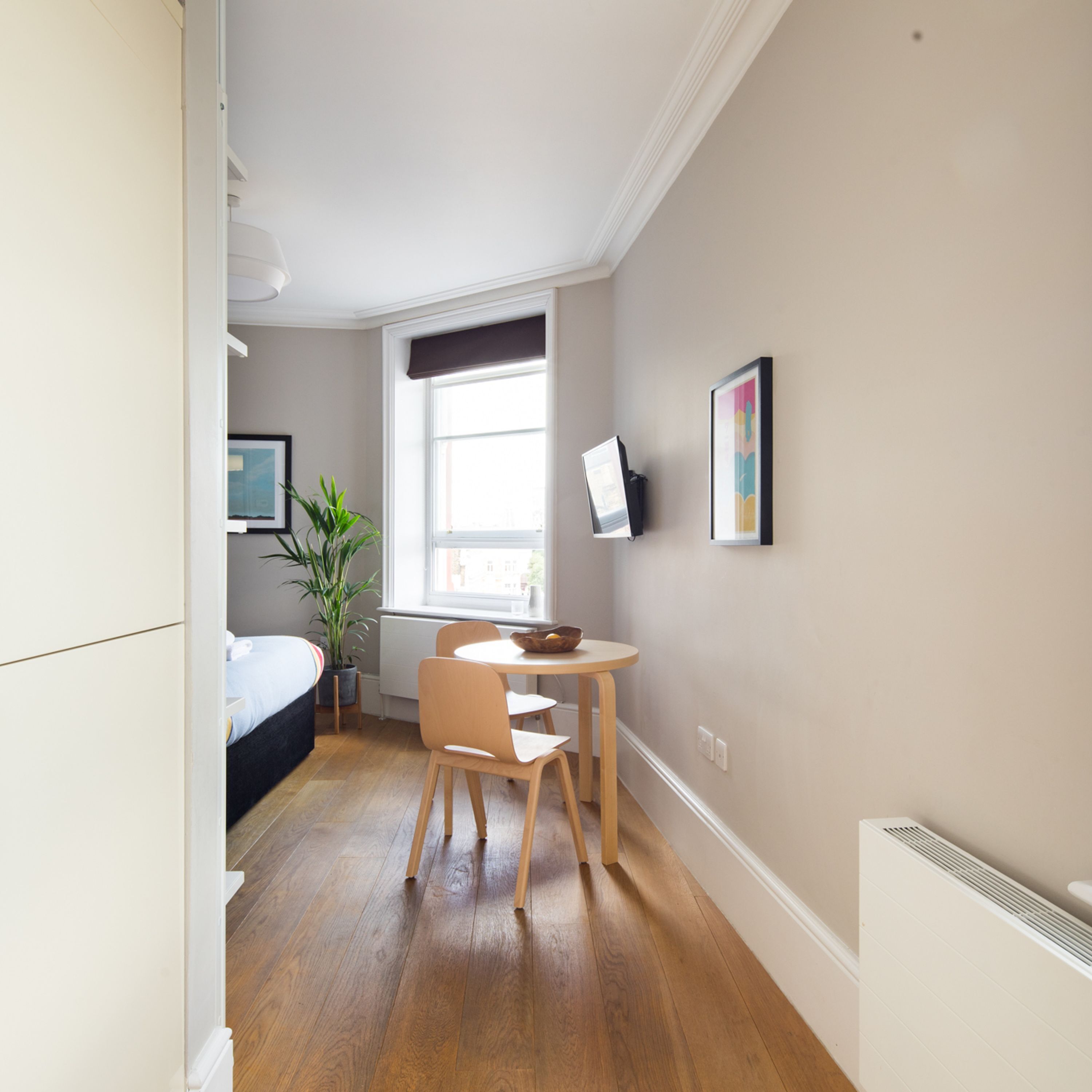 Quarto moderno com cama, mesa de cabeceira, planta em vaso e janela.