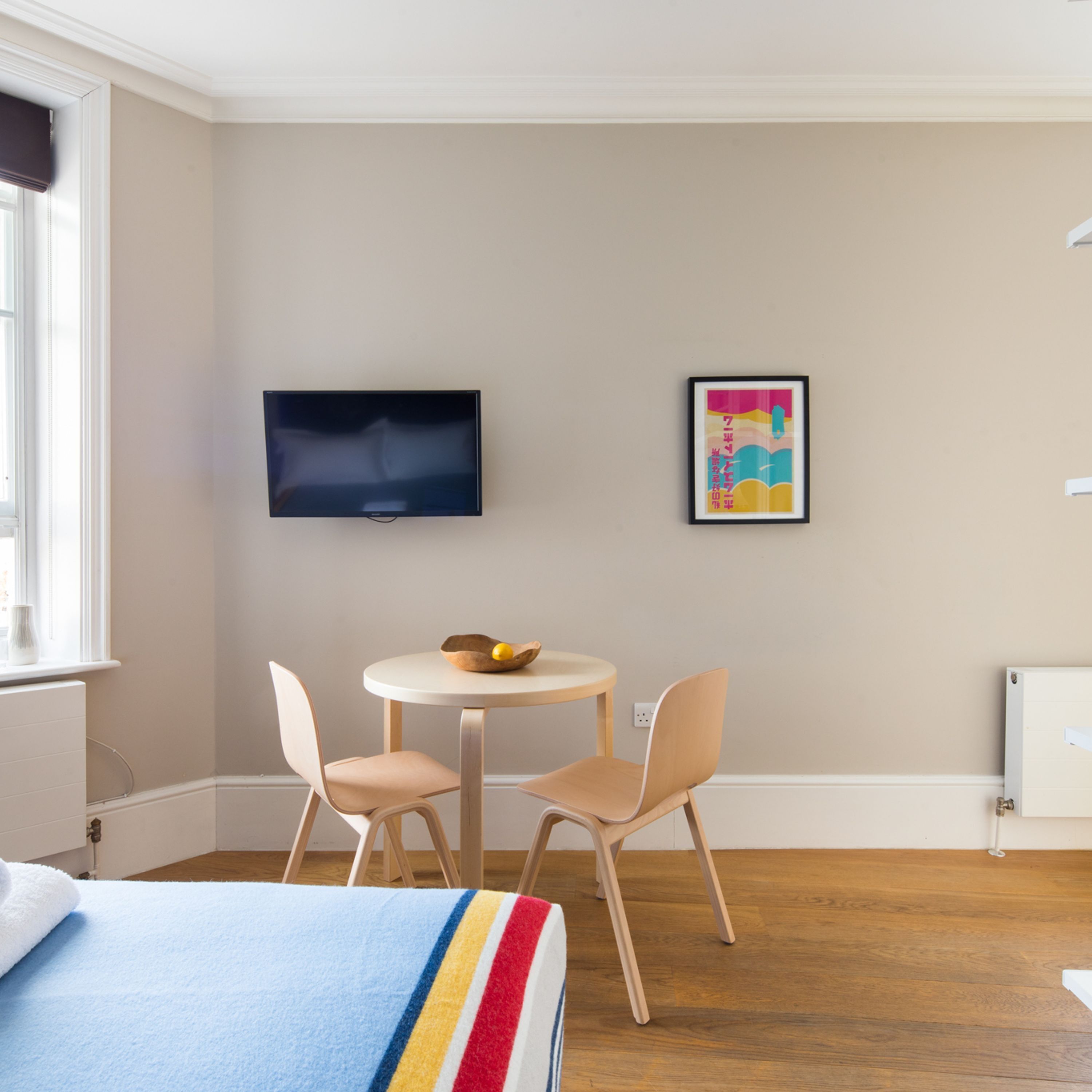 A hotel room with a bed, a round table with two chairs, a television mounted on the wall, and a framed picture.