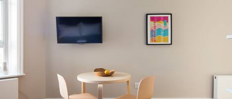 A hotel room with a bed, a round table with two chairs, a television mounted on the wall, and a framed picture.
