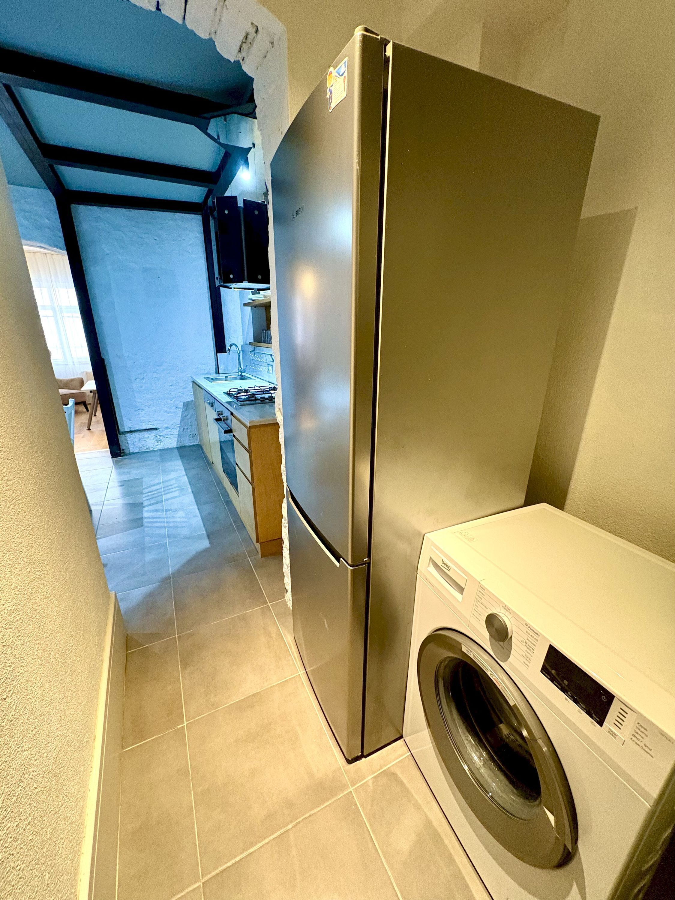 A compact kitchen with a stainless steel refrigerator and a front-loading washing machine.