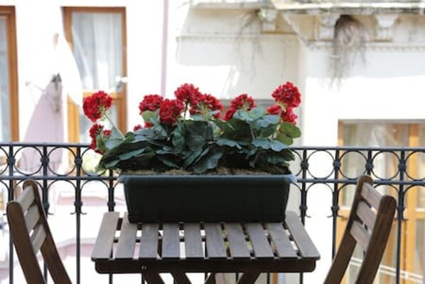 A balcony with a metal railing, a wooden bench, and a black planter with red flowers.