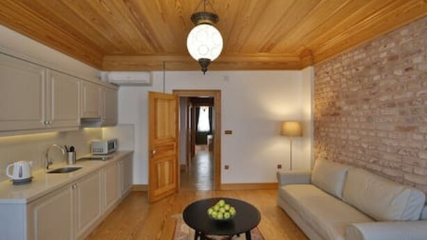 A kitchen with wooden cabinets, a microwave, and a sink. There is a round table with a bowl of fruit in the center of the room. A sofa is against a brick wall. - 401 Old City Brand New Spacious With Balcony (Istanbul)