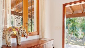 A wooden cabinet with a decorative elephant sculpture, a window with metal bars, and a view of palm trees outside. - Casa Para Familias en Ibiza (Sant Josep de sa Talaia)