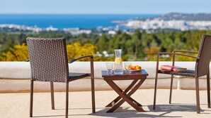 Two wicker chairs and a small table with drinks and a book on a balcony overlooking a scenic view. - Casa Para Familias en Ibiza (Sant Josep de sa Talaia)