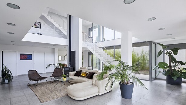 A spacious living area with a white sectional sofa, two armchairs, a coffee table, and a large potted plant. A staircase leads to an upper level, and the room has a modern design with large windows and a flat ceiling. - Garriguella Emporda Costa Brava (Garriguella)