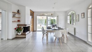 A modern kitchen with white cabinetry, a dining area with a white table and chairs, and a view through the glass door to the outside. - Garriguella Emporda Costa Brava (Garriguella)