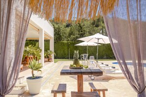 An outdoor patio with a table set for two, surrounded by potted plants and a pool area. - Villa Jesus in Ibiza (Santa Eulalia del Rio)