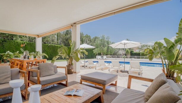 A covered outdoor seating area with a pool view, wooden furniture, and potted plants. - Villa Jesus in Ibiza (Santa Eulalia del Rio)