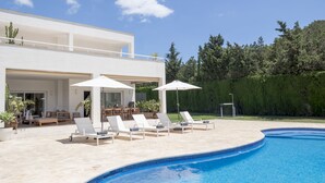 A modern pool area with lounge chairs and umbrellas, a clear blue sky, and a landscaped garden. - Villa Jesus in Ibiza (Santa Eulalia del Rio)