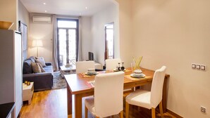 Un salon moderne avec un canapé, une table à manger et des chaises. On y trouve également un téléviseur, une lampe et une fenêtre avec des rideaux.