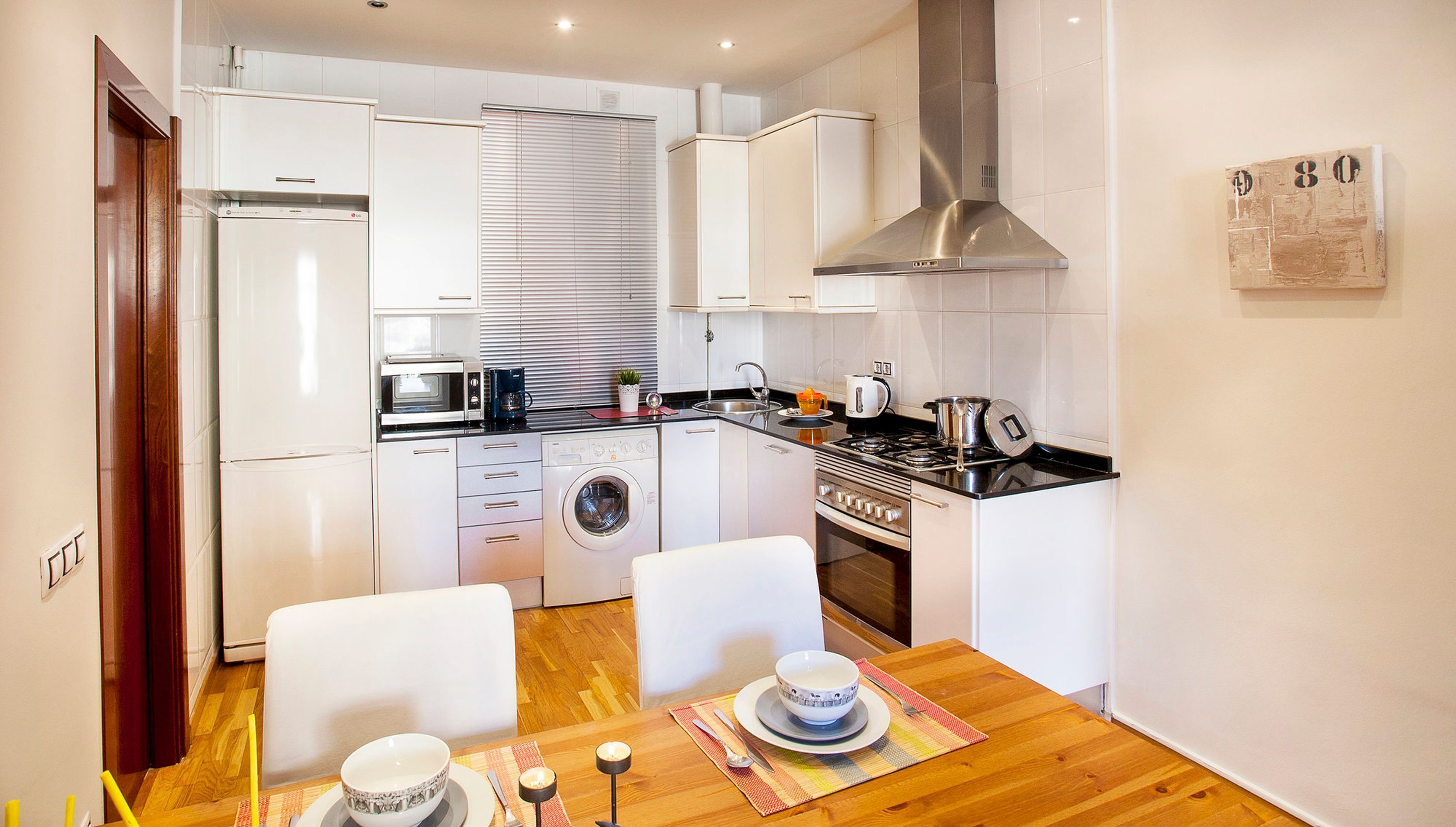 A compact kitchen with a microwave, coffee maker, sink, stove, and a dining area with a table set for two.