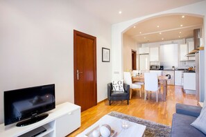A modern living room with a flat-screen TV, a sofa, a dining area with a table and chairs, and a kitchen with appliances. - Viladomat Eixample Apartment (Barcelona)