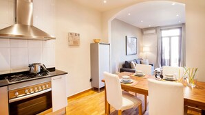 Une cuisine moderne équipée d’une cuisinière, d’un four et d’une hotte en acier inoxydable. On y trouve également un coin repas avec une table en bois, des chaises blanches et un canapé.