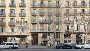 Un immeuble à plusieurs étages doté de balcons, d’un panneau indiquant un parking et de voitures garées.