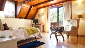 Ein Schlafzimmer mit Bett, Schreibtisch, Stuhl, Lampe und einem Balkon mit Vorhängen.