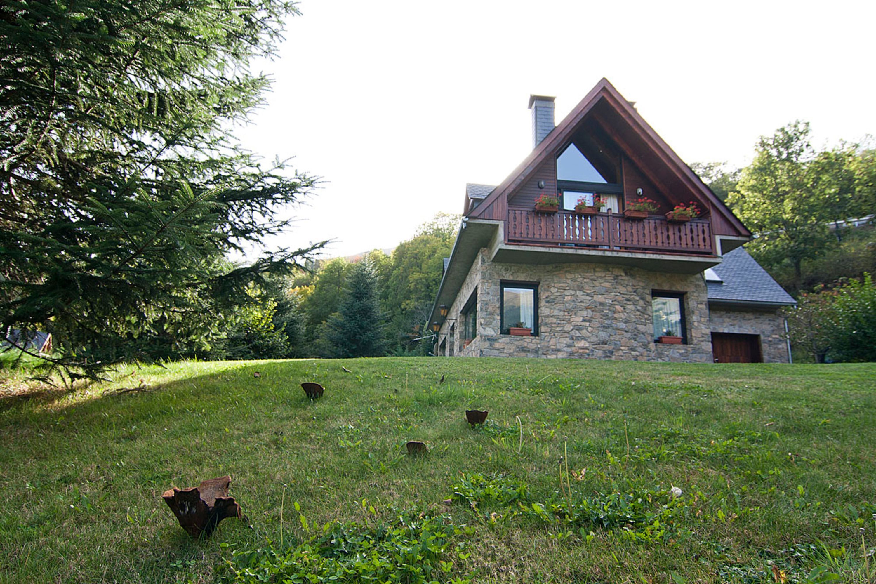 A stone house with a balcony, surrounded by a grassy area and trees.