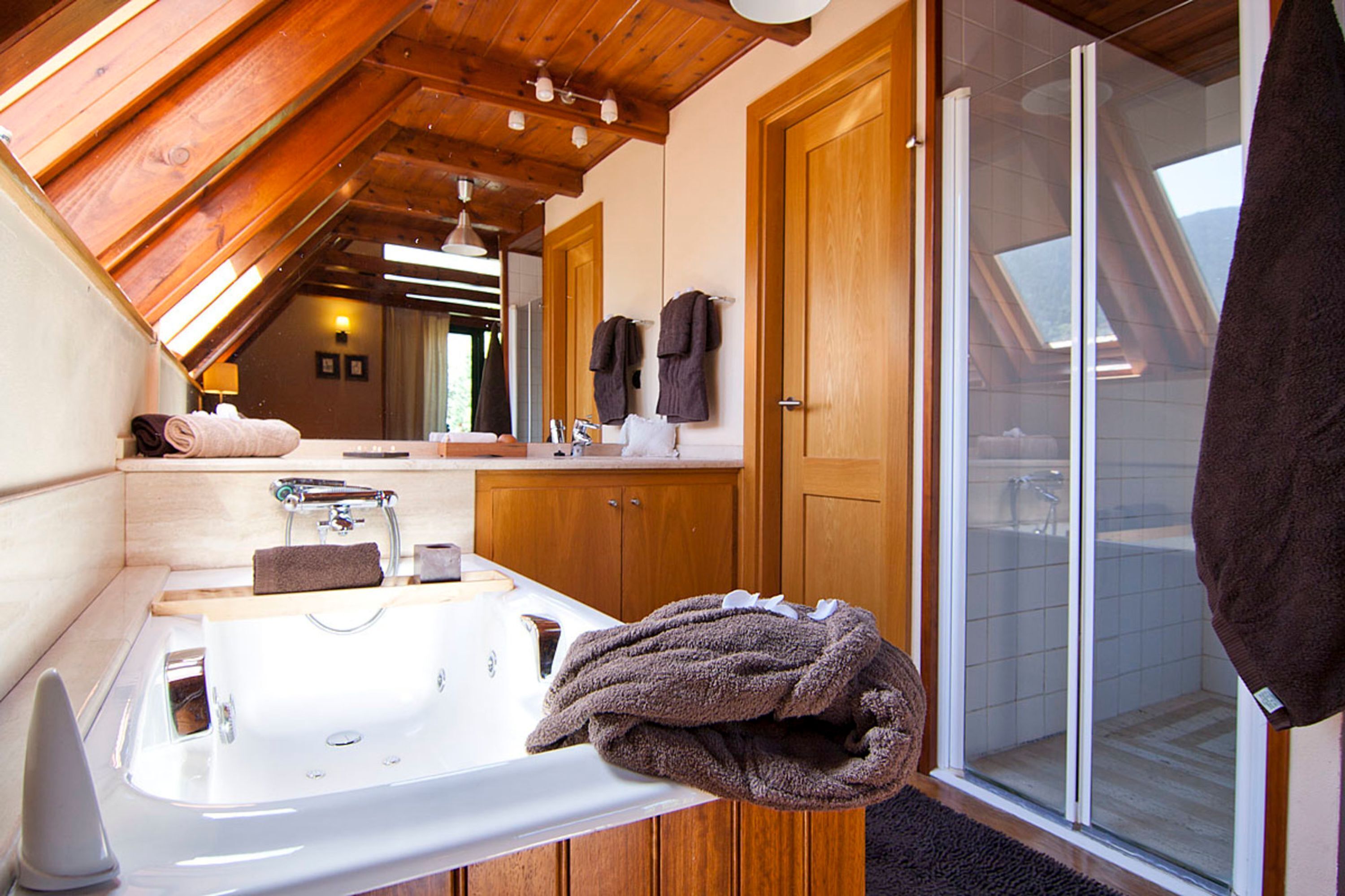 Une salle de bain avec un plafond en bois, un lavabo blanc, un miroir et une porte de douche en verre.