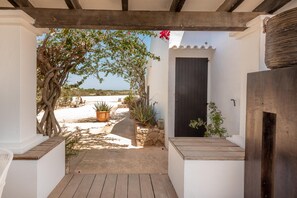 A covered patio with a wooden floor, white walls, a black door, and potted plants.
