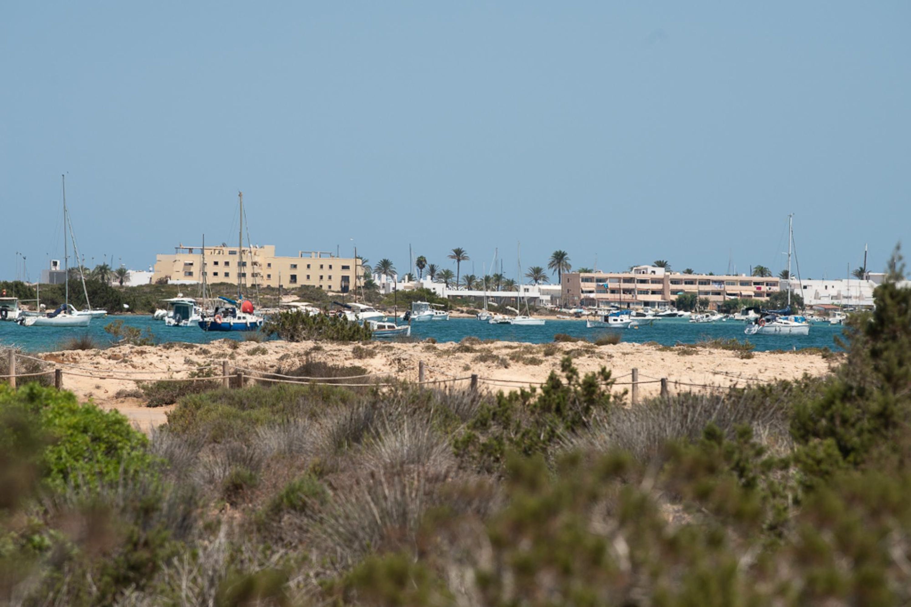 A coastal area with a sandy beach, several boats docked, and a large building in the background.