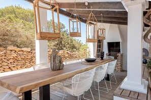 An outdoor dining area with a wooden table and white chairs, surrounded by stone walls and hanging lanterns. - Formentara in Formentera (Formentera)