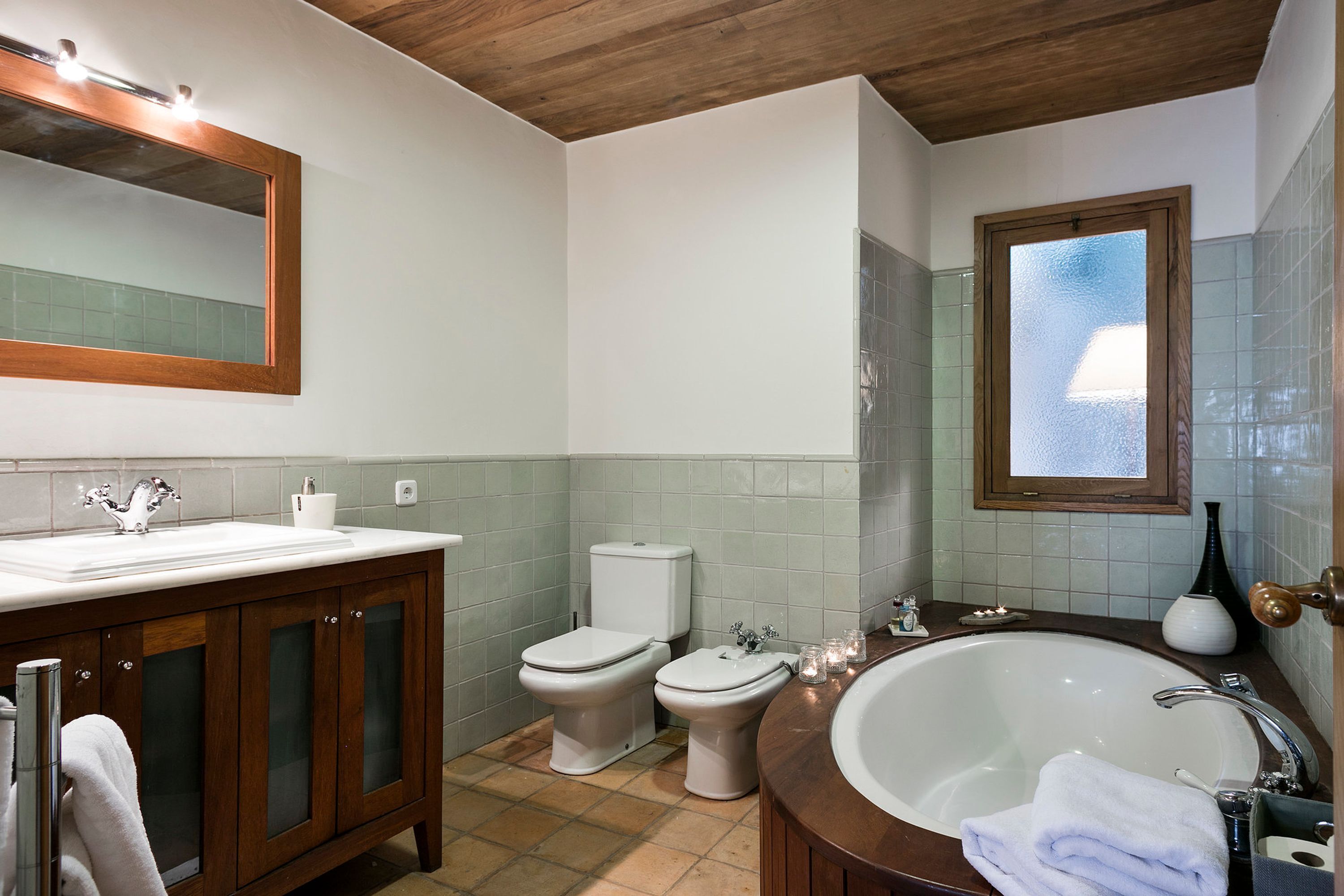A bathroom with a wooden vanity, two toilets, a large bathtub, and a mirror above the sink.