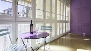 A room with a purple table and chairs, a bottle of wine, and a view through large windows. - Rambla Paris Apartment (Barcelona)