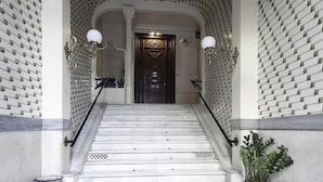 A grand staircase with a dark wooden door at the top, flanked by white walls with a repeating pattern. - Rambla Paris Apartment (Barcelona)