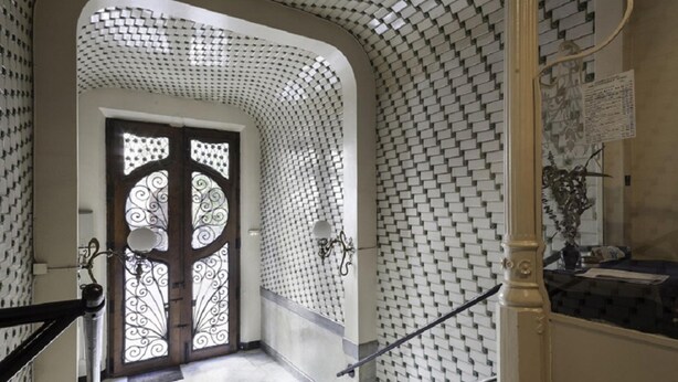 A hallway with a patterned tiled wall, a double door with intricate designs, and a staircase with a handrail. - Rambla Paris Apartment (Barcelona)