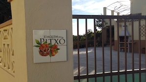 Un cancello con un cartello che recita "Joaquim Dela Pitxo" e vista su un cortile con un'area barbecue.