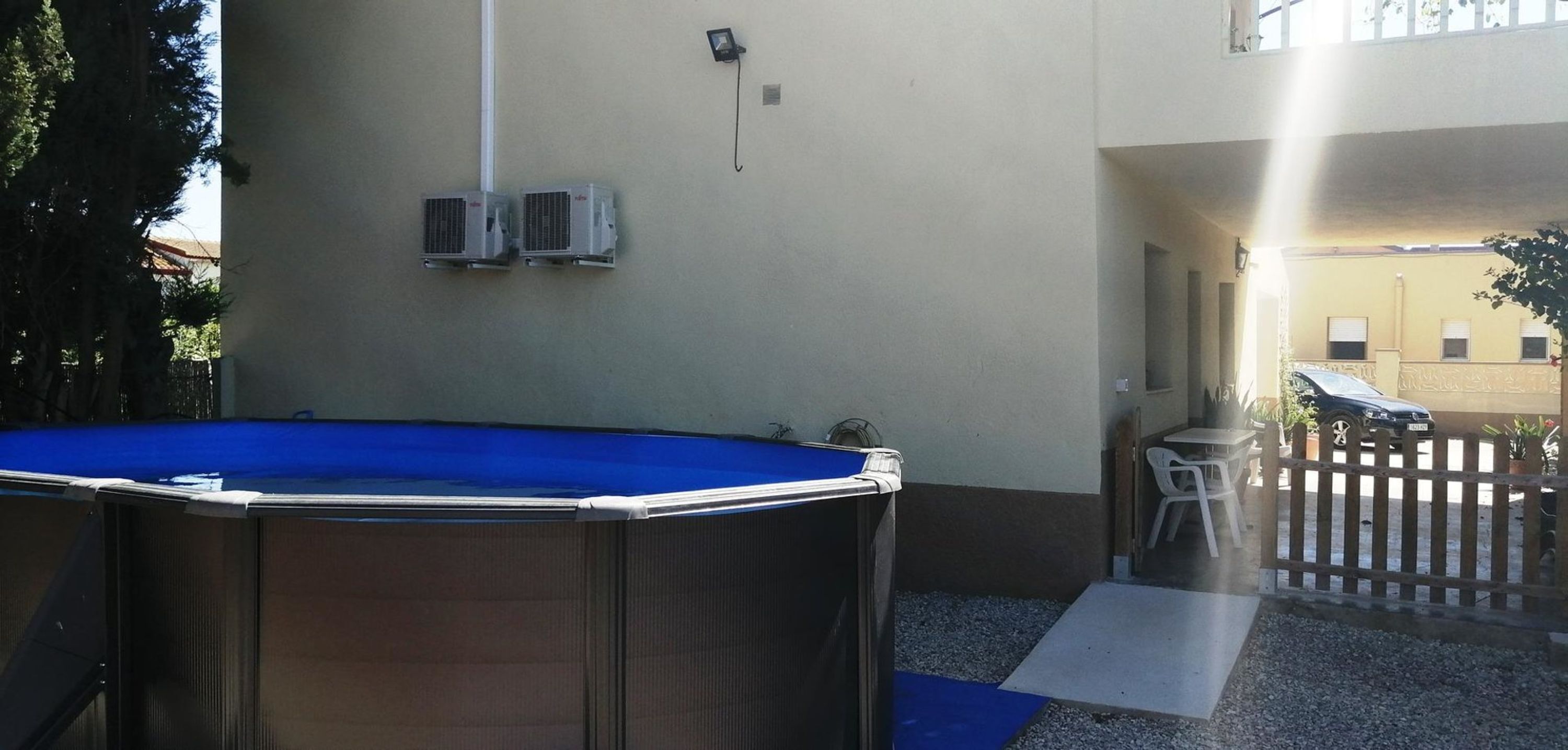An outdoor pool area with a blue pool, air conditioning units, and a wooden fence.
