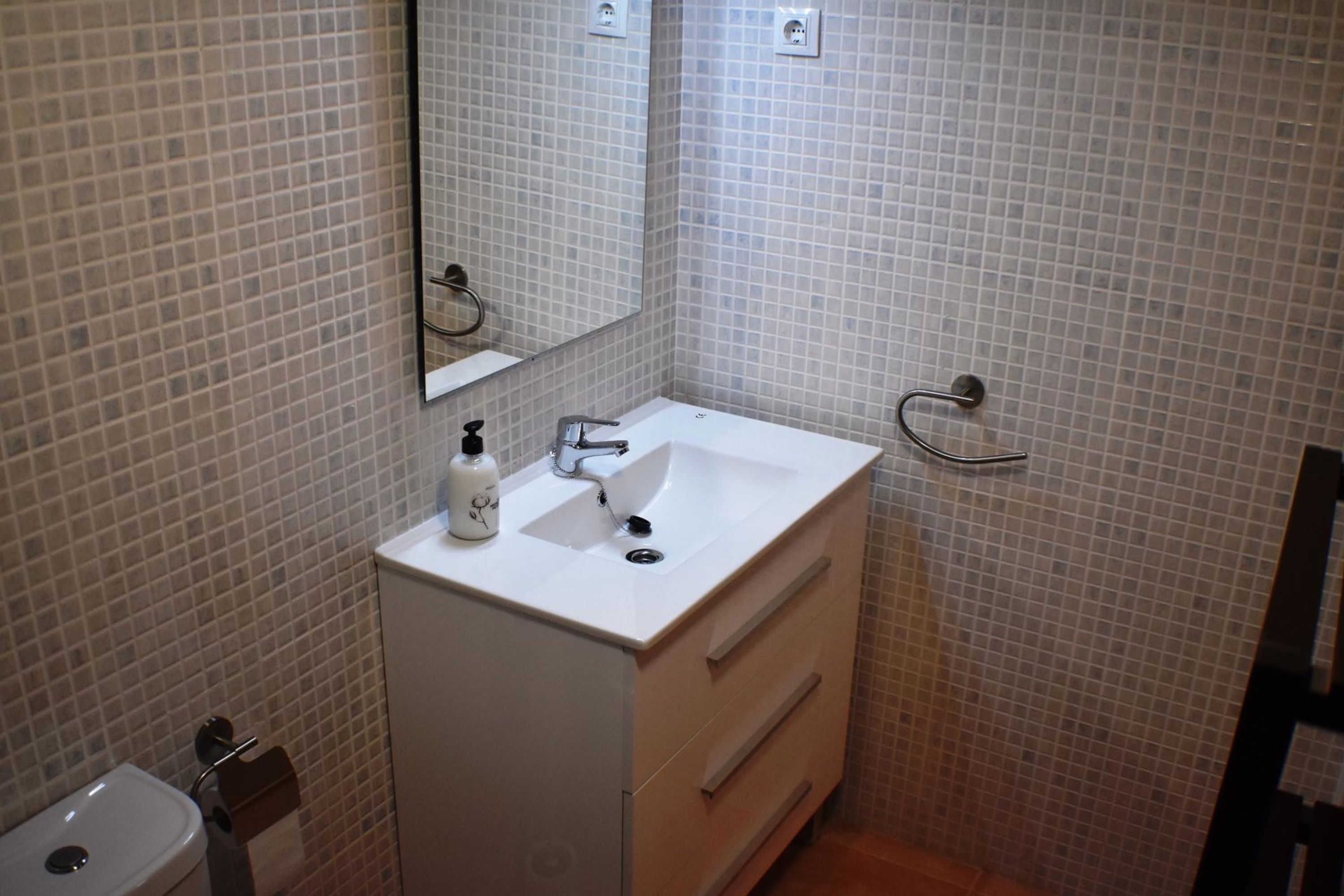 Un baño con un lavabo blanco, un espejo, un perchero para toallas y un inodoro.
