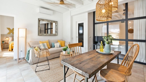A spacious living area with a wooden dining table, wicker pendant lights, and a large window with curtains. - Sant Mori- La Escala Boutique Apartment (Sant Mori)