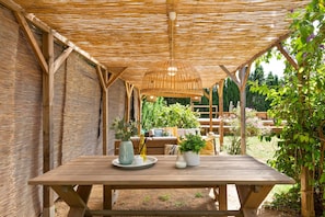 A wooden table under a thatched roof with potted plants and a hanging light fixture. - Sant Mori- La Escala Boutique Apartment (Sant Mori)
